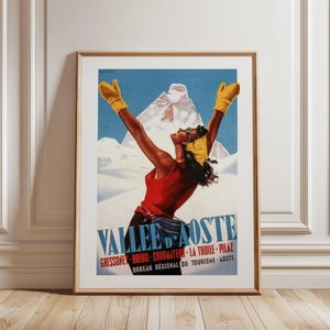 Op de afbeelding: Vintage reisposter in een gouden lijst. De poster toont een vrouw in een rode top en gele handschoenen met opgeheven armen, tegen een besneeuwde bergachtergrond. Tekst luidt "VALLEE D'AOSTE" en andere Italiaanse plaatsnamen.