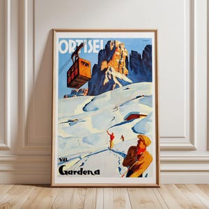 May include: A framed vintage travel poster depicting a ski resort. The image shows a cable car, snow-covered mountains, and skiers. The poster includes the text "ORTISEI" and "VAL Gardena".