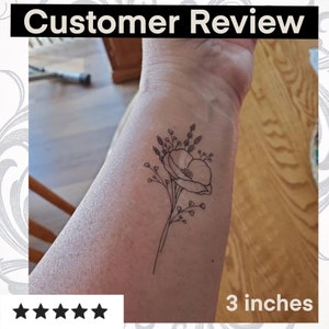 Puede incluir: Un tatuaje temporal en blanco y negro de una flor con una sola flor grande y flores m&aacute;s peque&ntilde;as que la rodean. El tatuaje mide 7,6 cm.