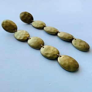 May include: A pair of long gold earrings with multiple oval-shaped beads. Each earring has five beads that are connected by a thin gold chain.