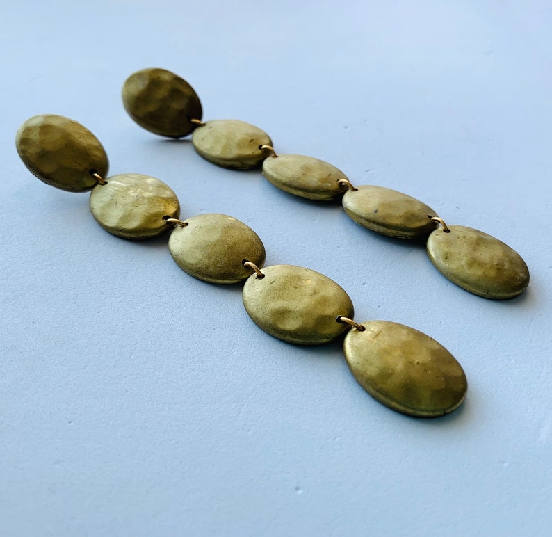 May include: A pair of long gold earrings with multiple oval-shaped beads. Each earring has five beads that are connected by a thin gold chain.