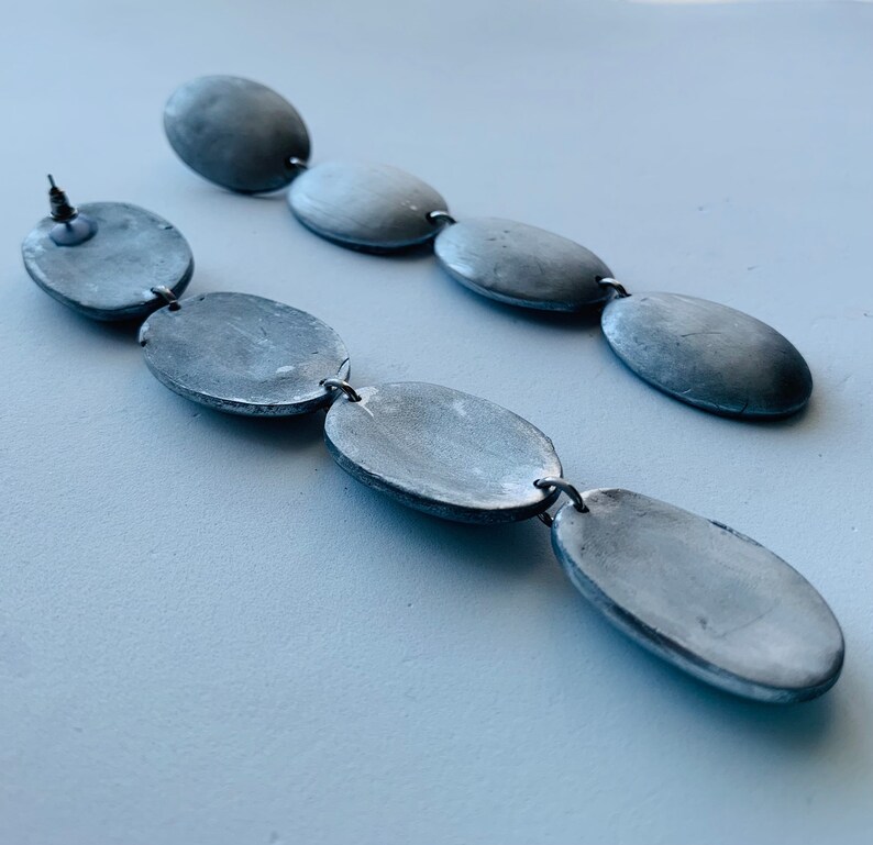 May include: A pair of long silver earrings with multiple oval-shaped beads connected by silver rings.