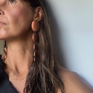 May include: A woman wearing a long, brown, copper-colored dangle earring with multiple round beads. The earring is on the right side of the image.