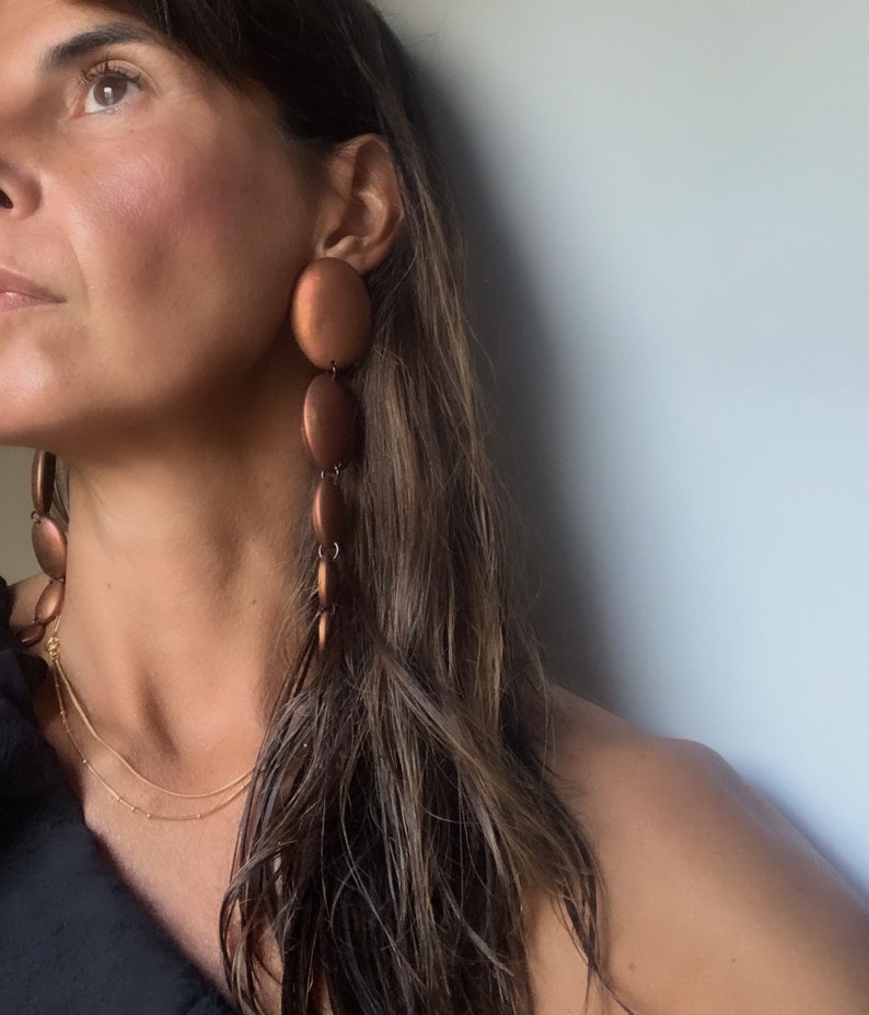 May include: A woman wearing a long, brown, copper-colored dangle earring with multiple round beads. The earring is on the right side of the image.