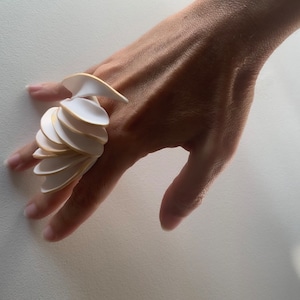 Op de afbeelding: Een witte keramische ring met gouden accenten. De ring is gemaakt van meerdere overlappende stukken die een uniek en modern ontwerp creëren.