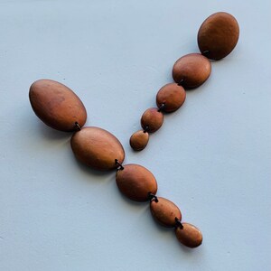 May include: A pair of long, dangling earrings with multiple oval-shaped beads. The beads are a metallic brown color and are connected by thin black string.