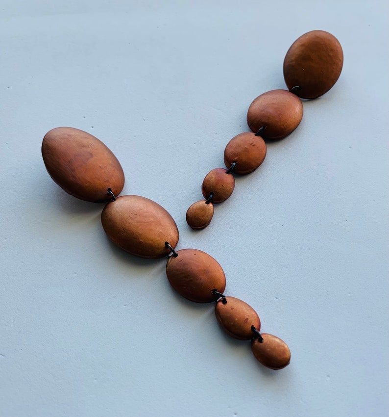 May include: A pair of long, dangling earrings with multiple oval-shaped beads. The beads are a metallic brown color and are connected by thin black string.