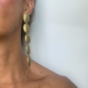 May include: Gold tone long drop earrings with multiple round discs. The discs are hammered and have a textured finish.