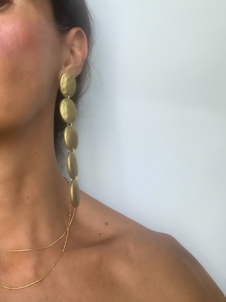 May include: Gold tone long drop earrings with multiple round discs. The discs are hammered and have a textured finish.