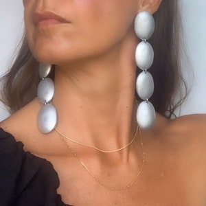 May include: Silver tone long drop earrings with multiple oval shaped links. The earrings are a statement piece and would be a great addition to any jewelry collection.