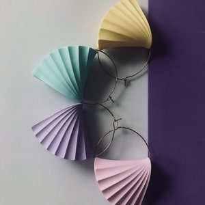 Pode incluir: Quatro pares de brincos de argola coloridos com um design em forma de leque. Os brincos são em tons de amarelo, azul, roxo e rosa.