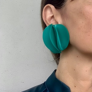 Könnte beinhalten: Ein Paar große, grüne, geometrische Ohrringe. Die Ohrringe sind aus einem glatten, kunststoffartigen Material gefertigt und haben ein einzigartiges, gefaltetes Design.