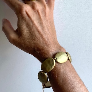 Pode incluir: Um bracelete dourado com elos de forma oval. O bracelete é feito de metal martelado e tem um fecho delicado de corrente.