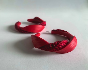 Peut inclure: Une paire de boucles d'oreilles créoles rouges avec un design de corde torsadée. Les boucles d'oreilles sont en matériau lisse et texturé.