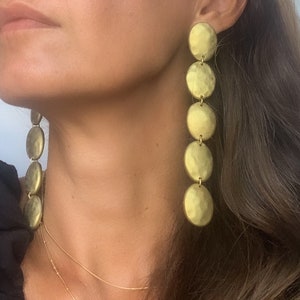 May include: Gold tone long drop earrings with multiple round discs. The discs are hammered and have a textured finish.