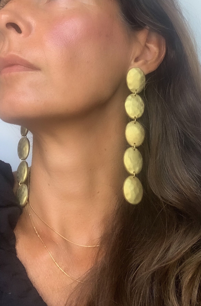 May include: Gold tone long drop earrings with multiple round discs. The discs are hammered and have a textured finish.
