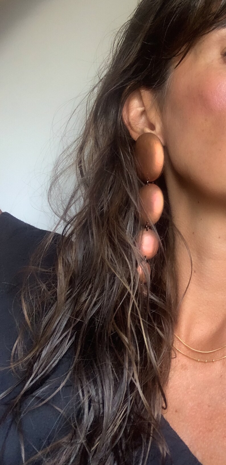 May include: A woman wearing a black top with a gold chain necklace and large, round, copper-colored earrings.