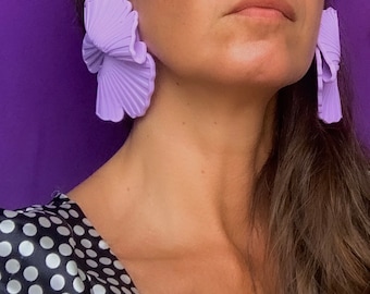 Può includere: Un paio di grandi orecchini statement di colore viola con un design piegato a forma di ventaglio. Gli orecchini sono realizzati in un materiale liscio e flessibile.