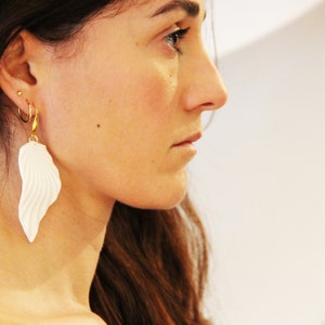 May include: A pair of white, textured, feather-shaped earrings with gold hoops and a gold chain.