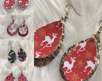 May include: A collection of four pairs of teardrop-shaped earrings featuring various patterns including red with white reindeer, gingerbread cookies, colorful holiday light bulbs, and red paisley with black and white stripes, all with metal hooks.
