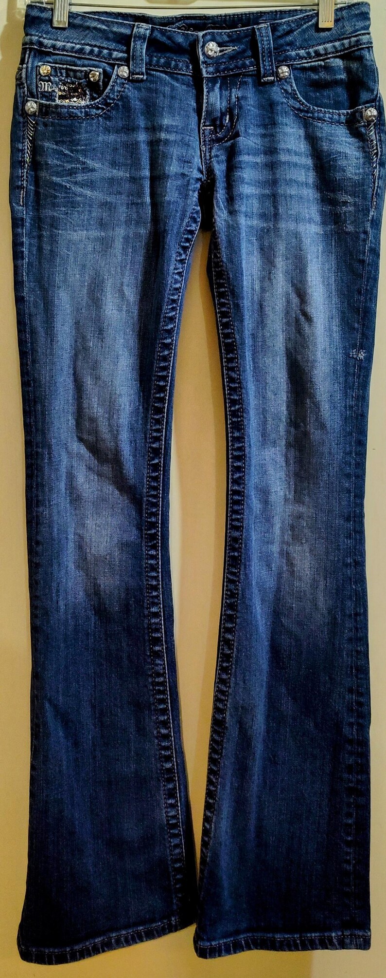 Op de afbeelding: Een paar donkerblauwe spijkerbroeken met een bootcut-poot. De jeans heeft een decoratief stikseldetail langs de naden en een klein versiering op de achterzak.