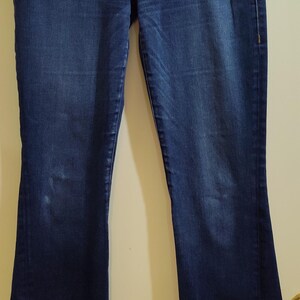 May include: Dark wash denim jeans with a bootcut leg. The jeans have gold-colored hardware, including rivets and a button. Decorative stitching in gold thread accents the pockets and side seams.