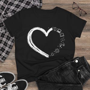 Könnte beinhalten: Schwarzes T-Shirt mit einem weißen Herzdesign mit Technologie-Symbolen. Das Herz enthält Bilder von Telefon, Laptop, Wolke, Glühbirne und Leiterplatte. Das T-Shirt wird mit einer schwarzen Jeans, einem karierten Hemd und Turnschuhen gezeigt.