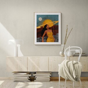 May include: A digital art print featuring a woman with a ring of planets around her head, standing in a desert landscape with a yellow sun and a white moon in the sky.