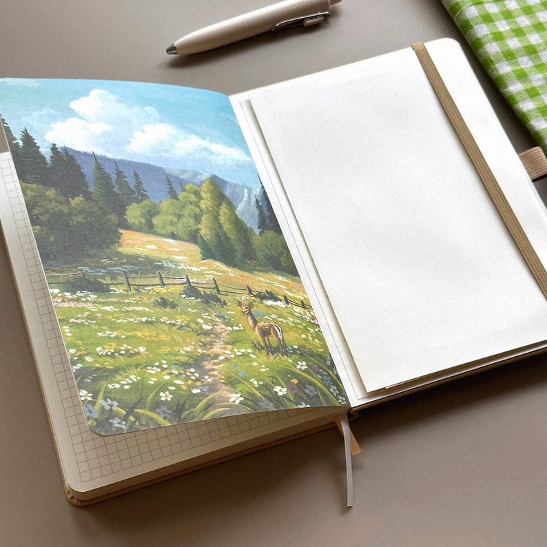May include: Open notebook with a landscape painting of a deer in a meadow. The painting features a path, fence, and trees under a blue sky. The notebook has a grid pattern on the left page and blank pages on the right. A pen rests above the notebook.