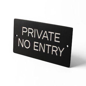 May include: Black rectangular sign with the words "PRIVATE NO ENTRY" in white, sans-serif font. The sign has two small holes, one on each side. The sign is angled slightly, showing its thickness.