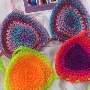May include: Close-up of four handmade crochet bikini tops in vibrant colors. The tops feature a variety of hues, including pink, purple, blue, green, and orange. Each top has a unique color gradient and design, showcasing the craftsmanship.