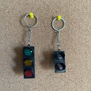 May include: Two black traffic light keychains with red, yellow, and green lights. Each keychain has a silver ring and chain.