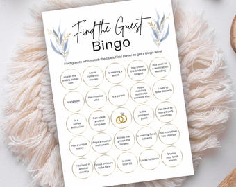 May include: A white Find the Guest Bingo game card with blue and gold floral accents. The game includes various prompts for guests to match, such as "Shares the bride's zodiac sign" and "Loves romantic movies."