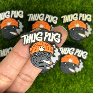 May include: A collection of black and gray pug charms, each wearing an orange beanie with a marijuana leaf and smoking a cigarette. The text "THUG PUG" is above each pug's head in white letters.