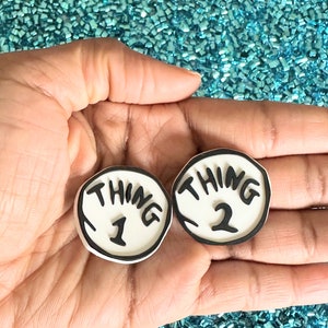 May include: Two white round buttons with black outlines and the words "Thing 1" and "Thing 2" in black.