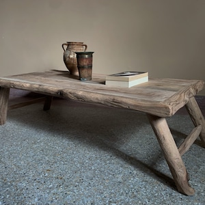 K&ouml;nnte beinhalten: Rechteckiger Couchtisch aus hellem Holz mit schr&auml;gen Beinen. Zwei antike Vasen und ein Buch liegen auf der Oberfl&auml;che. Der Tisch hat eine nat&uuml;rliche, unbehandelte Optik.