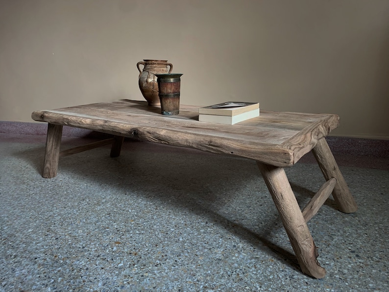 K&ouml;nnte beinhalten: Rechteckiger Couchtisch aus hellem Holz mit schr&auml;gen Beinen. Zwei antike Vasen und ein Buch liegen auf der Oberfl&auml;che. Der Tisch hat eine nat&uuml;rliche, unbehandelte Optik.