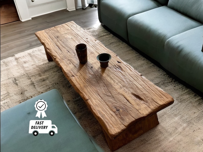 May include: A rustic, rectangular wooden coffee table with a natural edge. The table is a warm brown color and has visible wood grain. Two small, dark brown ceramic cups sit on the table. The image also includes a light blue ottoman and a green sofa.