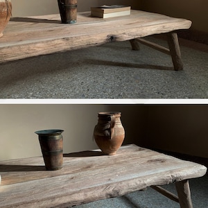 K&ouml;nnte beinhalten: Ein rustikaler Couchtisch aus Holz mit nat&uuml;rlicher Oberfl&auml;che. Der Tisch hat eine rohe Kante und schr&auml;ge Beine. Eine Vase aus Metall und Holz und ein kleines Buch liegen auf dem Tisch. Der Tisch ist etwa 152 cm lang.