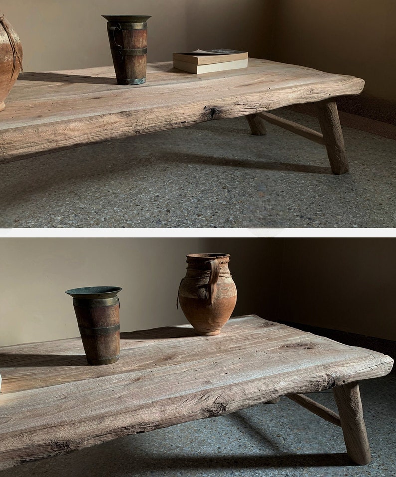 K&ouml;nnte beinhalten: Ein rustikaler Couchtisch aus Holz mit nat&uuml;rlicher Oberfl&auml;che. Der Tisch hat eine rohe Kante und schr&auml;ge Beine. Eine Vase aus Metall und Holz und ein kleines Buch liegen auf dem Tisch. Der Tisch ist etwa 152 cm lang.