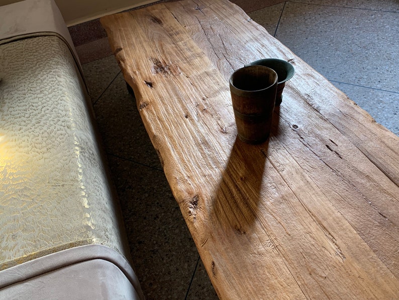 May include: A rustic, light brown wooden coffee table with a natural edge. Two small, dark brown wooden cups sit on the table. The table has visible wood grain and knots, and is next to a light-colored sofa.