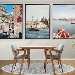 May include: Three framed prints of scenes from Valletta, Malta. The first print shows a narrow street with colorful buildings and a bridge. The second print shows a harbor with a sailboat and a church in the background. The third print shows a church with a red dome and a view of the harbor.