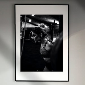 May include: Black and white photo of a woman lifting weights in a gym. She is wearing a black sports bra and has her hair pulled back in a ponytail.