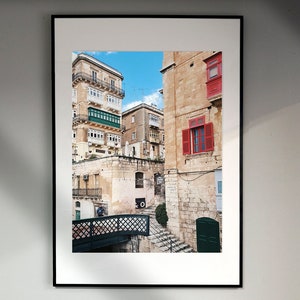 May include: A framed photograph of a narrow street in a European city. The buildings are made of stone and have red and green window shutters. A small bridge crosses the street in the foreground.