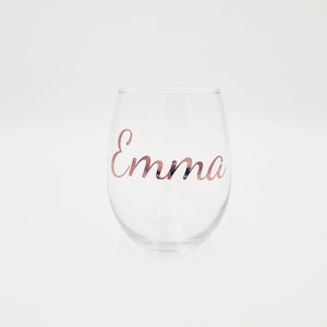 May include: A clear glass wine glass with the name "Emma" written in rose gold lettering.