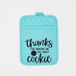 May include: A turquoise blue pot holder with the text "thanks for making me one smart cookie" in black lettering. A black and white cookie graphic is included in the text.
