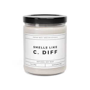 May include: A glass jar candle with a black lid and a white label that reads "PAPER BAG DESIGN STUDIO", "SMELLS LIKE C. DIFF", "NATURAL SOY WAX", "9 oz/255g", and "SOHR BURN TIME".