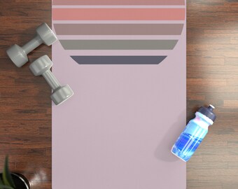 May include: A purple yoga mat with a retro sunset design. The mat is on a wooden floor with a water bottle and two grey dumbbells.