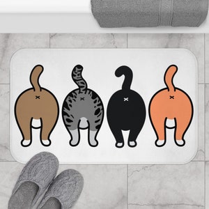 May include: A white bath mat with four cartoon cats facing away from the viewer. The cats are brown, gray, black, and orange. Each cat has a tail and a white 'X' on its rear end.