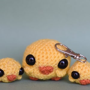 May include: Three crocheted yellow chicks with black eyes and orange beaks. The middle chick is larger and has a silver keychain attached.